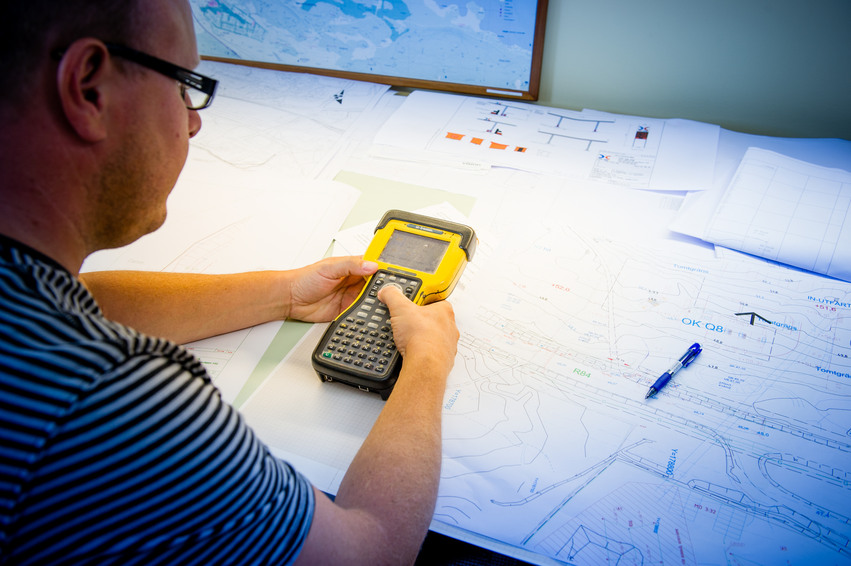 En man sitter vid ett skrivbord och planerar framför stora kartor.