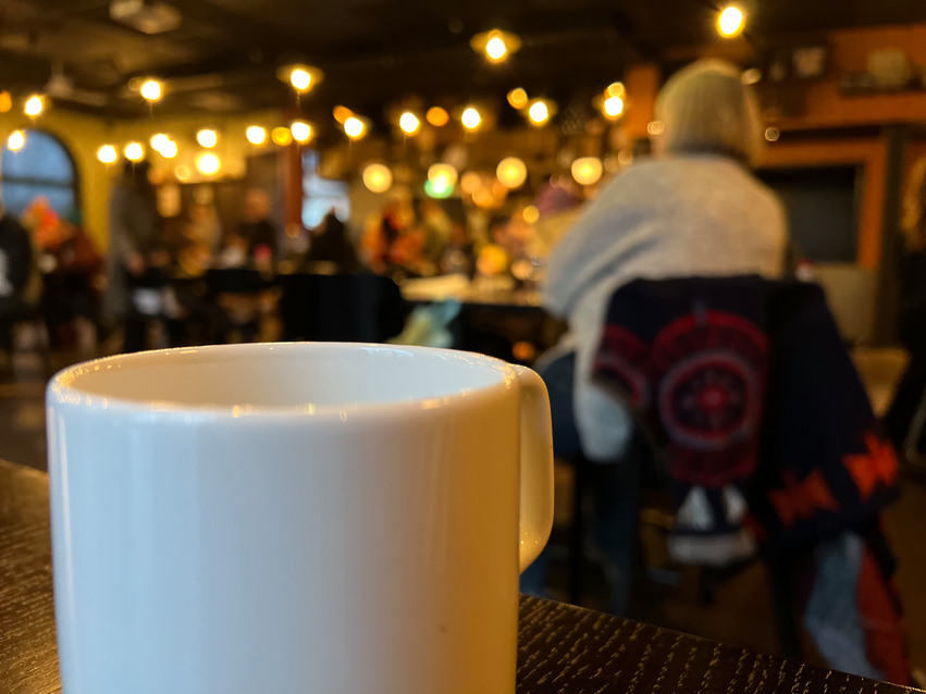 Kaffekopp i förgrunden och människor i bakgrunden.