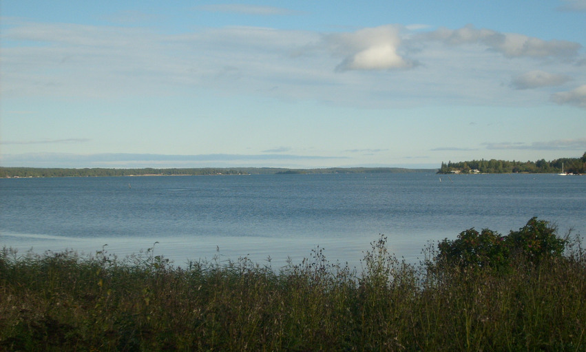Utsikt från strandkanten över havet med landområden i horisonten.