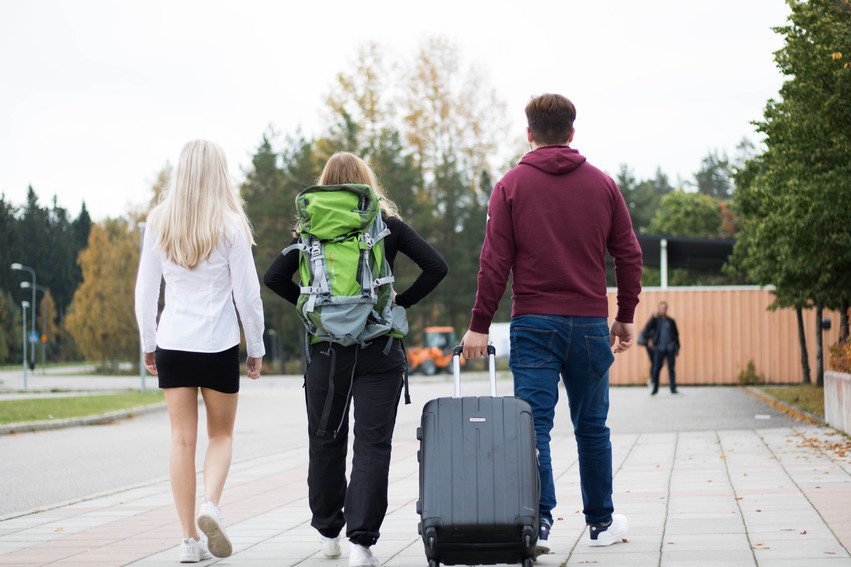 Tre elever går med ryggsäck och rullväska.