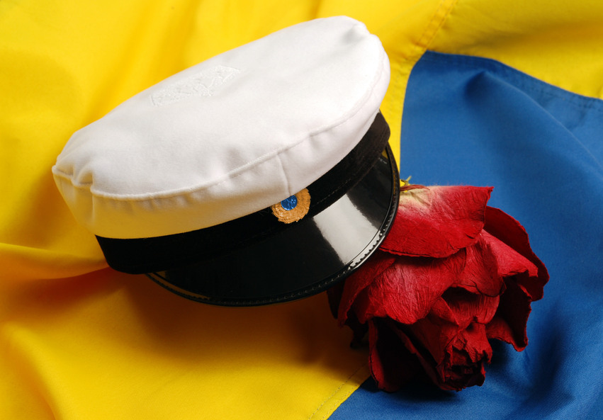 Närbild på en svart och vit studentmössa och en röd ros som ligger på svenska flaggan.