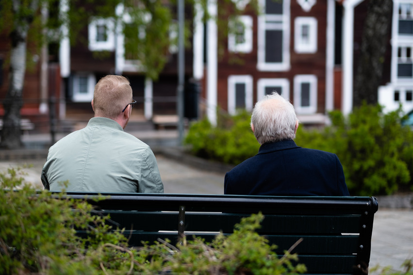 Två personer sitter på en parkbänk och kollar på sjöbodarna i Hudiksvall