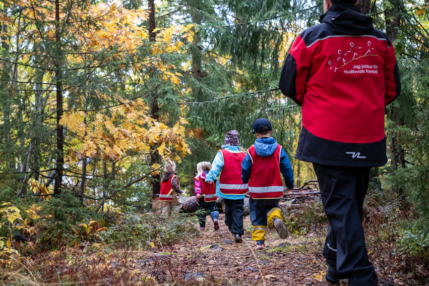 En förskollärare och fyra barn promenerar i en skog