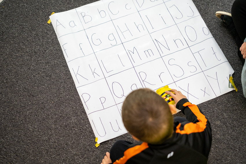 En barn leker med en gul leksak på en matta med alfabetet på