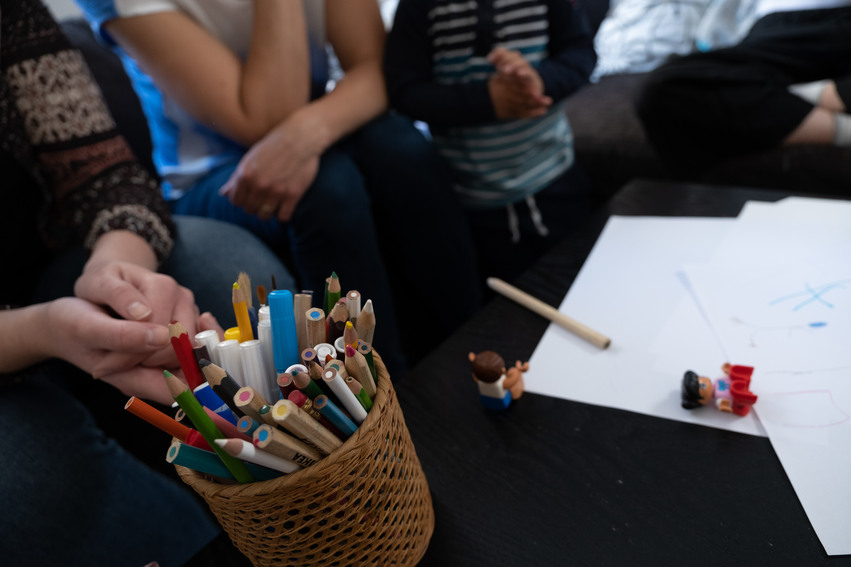 Vuxna och barn sitter vid ett bord och ritar.