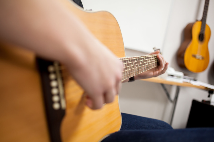 Närbild på en gitarr som en elev spelar på.