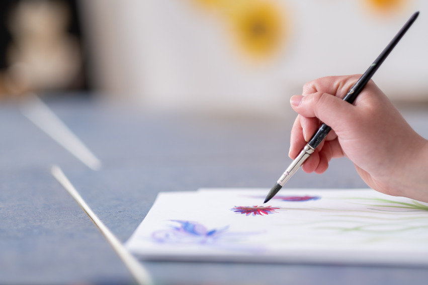 Närbild på en elev som sitter med en pensel i handen och målar på en vit duk.
