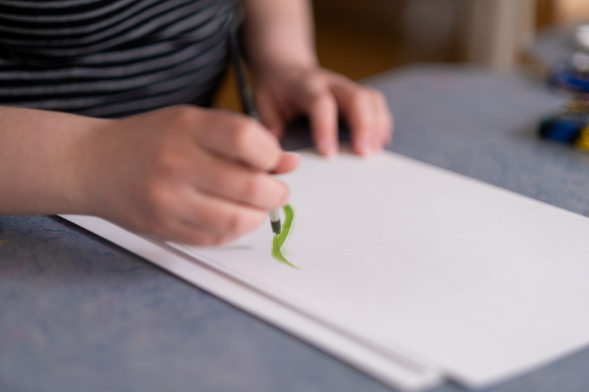 En elev sitter och målar med grön färg på ett vitt papper.