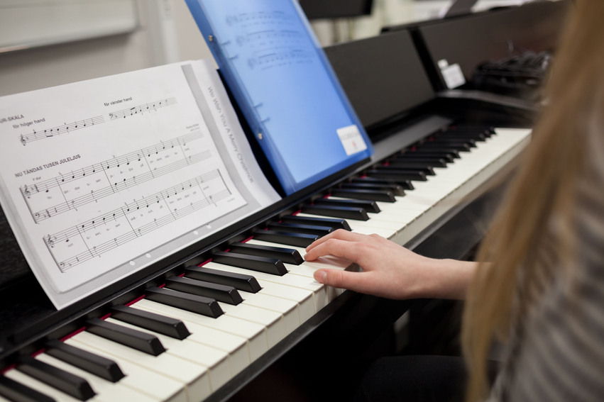 Närbild tagen på ett piano som en elev spelar på. Ett papper med noter syns på bilden.