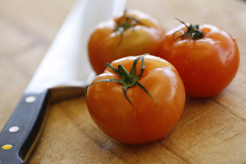 Närbild tagen på tre stora tomater och en kökskniv som ligger på en skärbräda.
