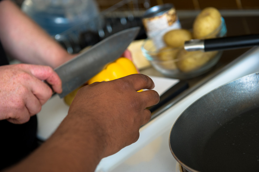 Närbild på en ur personalen och en boende som hjälps åt att laga mat. En håller i en stor gul paprika och den andra skär.