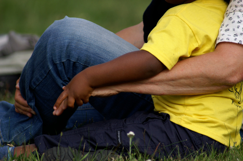 En person sitter och håller om ett barn på en grön gräsmatta.