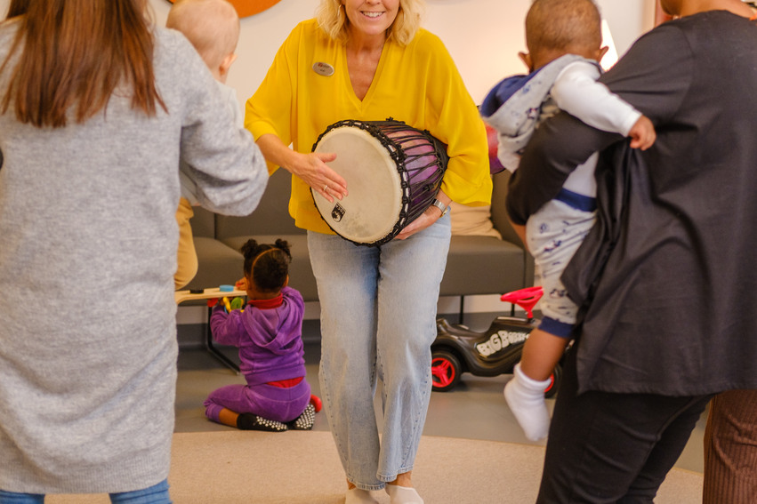 Föräldrar och barn dansar till en trumma som spelas av en personal. 