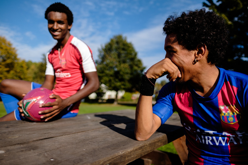 Två killar ombytta för att spela fotboll sitter vid några utebänkar i Borgarparken. Den ene sitter på bordet och håller i en rosa fotboll.
