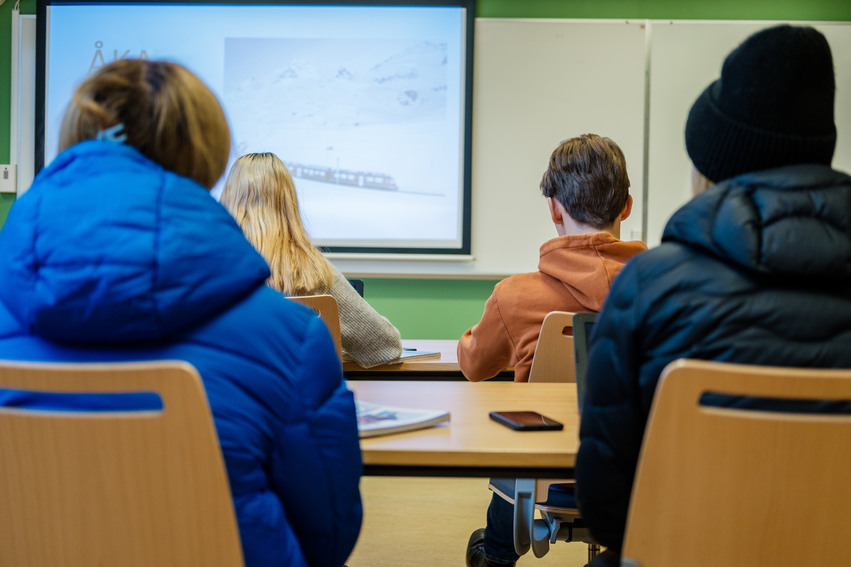 fyra elever sitter i ett klassrum och tittar på en skärm. 