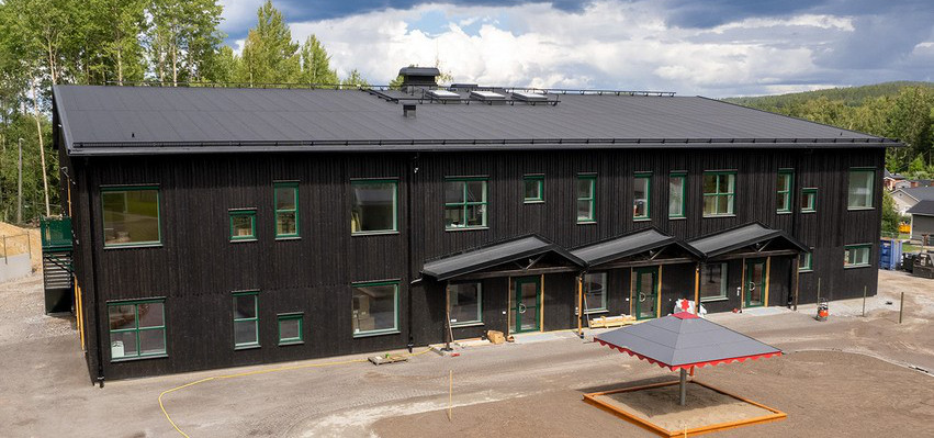 Linfröets förskolebyggnad med svart träfasad och utegård med sandlåda.