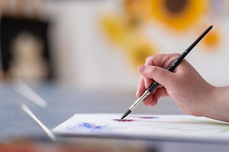 Närbild på en hand som håller i en pensel och målar.