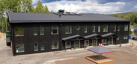 Linfröets förskolebyggnad med svart träfasad och utegård med sandlåda.